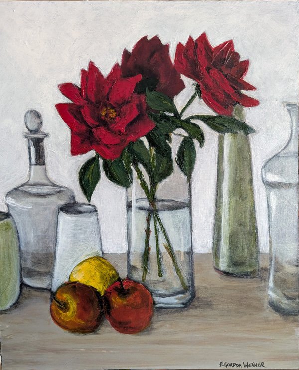 very dark red roses in a vase with other glassware, two apples and a lemon