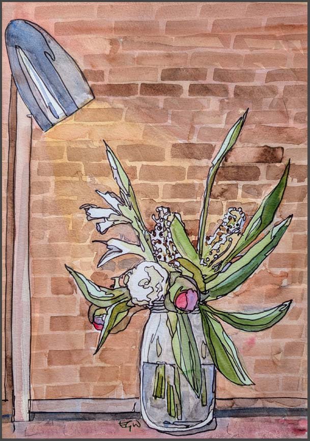 In front of a brick wall sits a glass jar full of flowers with a lamp shining on them.